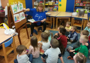 Dzieci siedzą przed tablicą, oglądają ilustracje do legendy „O smoku wawelskim”, nauczycielka wskazuje ilustrację smoka